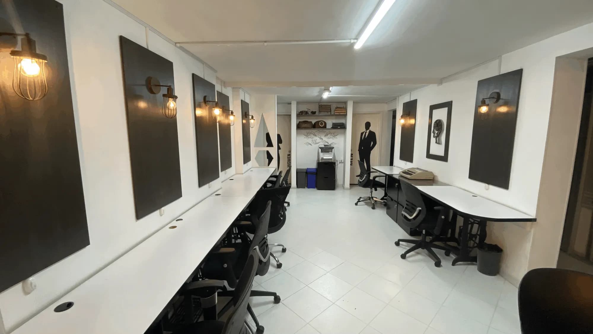 Zona de hot desk con escritorios largos y lámparas de pared